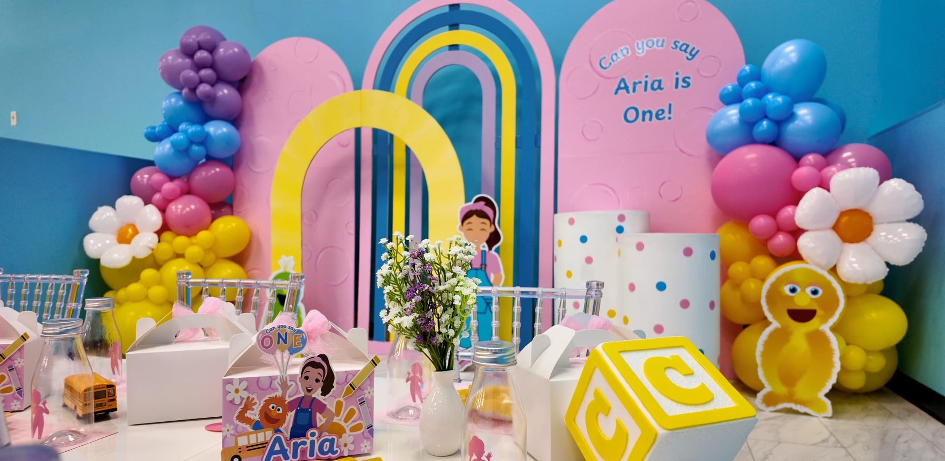 Ms. Rachel-themed first birthday party setup at Kidz Kastle in Warwick, RI, with pastel balloon garlands, personalized signage, and themed table decor for Aria’s celebration.