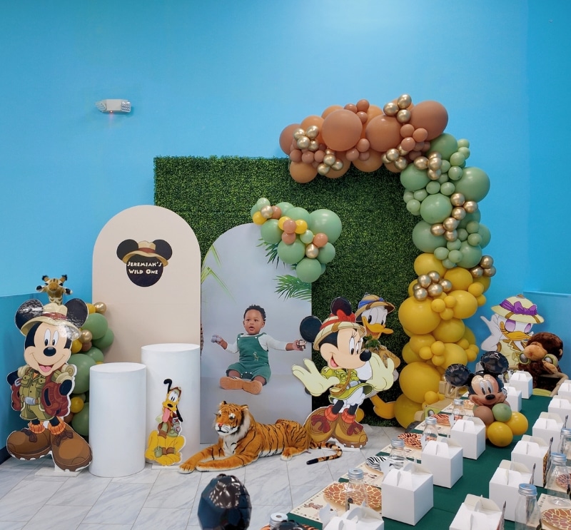 Vibrant Mickey Safari Kouture party theme featuring a personalized child photo backdrop and custom balloon garland at Kidz Kastle, Rhode Island.